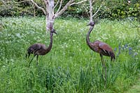 Deux sculptures d'oiseaux en métal dans un pré de fleurs sauvages.