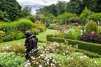 Une statue d'amants enlacés se tient dans un jardin à la française, avec des parterres d'arbustes et de vivaces, dont Rosa 'Little White Pet', Rosa 'Kent' et Sedum spectabile.