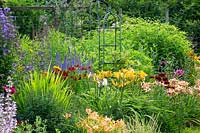 Parterre de fleurs coloré avec des oblisques métalliques. Les plantes comprennent Hemerocallis, Helenium, Veronicastrum, Rudbeckia hirta 'Cappuccino' et Echinops.