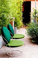 Deux chaises sur terrasse carrelée par l'entrée de la maison, les plantes de bambou dans les auges fournissent un écran