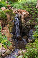 Petite cascade artificielle dans les rochers avec des plantes dans le jardin japonais.