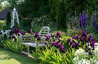 Le banc de Lutyens se dresse devant un parterre de fleurs herbacées aux iris violets profonds, aux delphiniums et à un obélisque blanc.