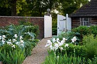 Chemin de gravier menant à de grandes portes blanches dans un jardin de campagne clos de murs.