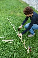 Mettre des pieux dans le sol en préparation pour faire une clôture pour les parterres de saules tissés