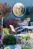 Miroir circulaire sur cabanon, entouré de plantes d'intérêt saisonnier dans le jardin d'automne.