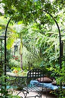Vue de la terrasse avec table à manger et mélange de plantes tropicales, y compris les palmiers, les fougères et les bégonias.