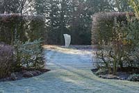 Sculpture connue sous le nom de voile, derrière Carpinus betulus - haie de charme au début de la gelée du matin.