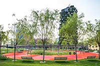Vue sur le parc public avec de jeunes arbres et des bancs autour d'une aire de jeux, en arrière-plan le Bosco Verticale - forêt verticale - par l'architecte Stefano Boeri
