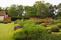 Jardin de campagne avec des écrans en acier corten, de vastes parterres de fleurs vivaces et des dômes topiaires sur la pelouse