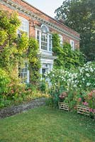Vue sur le jardin avant, avec pelouse, chemin pavé, Rosa - Rose et Alstroemeria standard avec des supports de plantes en bois miniature, d'époque maison avec des arbustes muraux