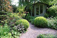 Jardin de la petite ville ombragée avec parterres de fleurs mixtes et Buxus - Boîte - topiaire près du chemin de gravier vers le pavillon d'été