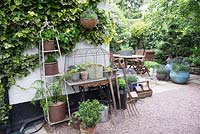 Affichage de pots et d'outils de jardin avec table de couture contre un mur de maison couvert de Hedera - Ivy, au coin d'un patio avec coin salon et plantation de pots