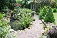 Jardin de la petite ville ombragée avec étang, chemin de gravier vers le pavillon d'été et Buxus - Boîte - cônes topiaires marquant l'entrée de la pelouse