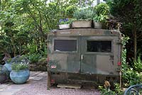 Vieux véhicule militaire inhabituel utilisé comme abri dans un petit jardin ombragé