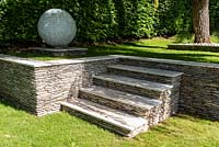 Jardin surélevé avec mur de soutènement en granit et marches et grand ornement globe