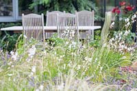 Gaura lindheimeri, Lavandula - Lavandes et herbe Stipa tenuissima dans un parterre de fleurs avec table et chaises en bois derrière