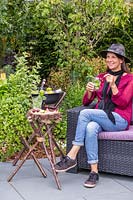 Femme se détendre et prendre un verre sur un patio en ardoise à côté d'un trio de structures de trépied - un planteur de menthe, une petite table de boissons et un refroidisseur de boissons