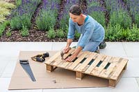 Femme utilisant des clous et un marteau pour fixer des morceaux de bandes de bois étroites pour combler les lacunes de la palette.