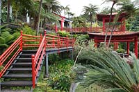 Jardin d'inspiration orientale inférieur avec mains courantes en bois peintes en rouge, situé dans un jardin tropical