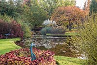 Sculptures de héron de Cotinus coggyria 'Royal Purple' - Sculptures de Smokebush et de cygne dans le parterre de fleurs d'Hylotelephium 'Herbstfreude' - Sedum 'Autumn Joy' - à côté du lac