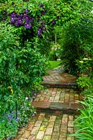 Chemin de brique à travers l'arche menant à la pelouse, avec Clematis viticella 'Etoile Violette' au-dessus - Journée des jardins ouverts, Double Street, Framlingham, Suffolk