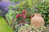 Pot à huile en céramique dans un parterre de fleurs d'Erigeron karvinskianus, eryngiums, roses, heuchera et catmint