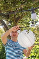Homme fixant une lanterne en papier blanc sur les ampoules dans la chaîne légère