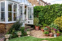 Petit jardin avec véranda attenante à la maison ouvrant sur un petit patio avec des plantes en pot