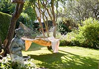 Grand hamac avec des couvertures accroché entre les arbres dans le jardin, sculpture en premier plan
