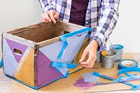 Woman remove masking tape pour révéler une boîte en bois peinte dans un motif géométrique multicolore