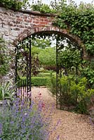 Une arche fermée en fer forgé dans un mur de manivelle serpentine ou froissée avec vue sur un jardin au-delà