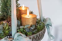 Détail de l'arrangement de l'Avent suspendu avec bougies en or, sapin de Noël miniature et feuillage d'eucalyptus et de Hebe.