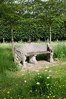 Banc en pierre antique et tilleul pleached derrière dans un jardin de pays avec pré de fleurs sauvages.