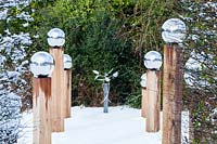 Avenue de poteaux en bois surmontés de globes en acier inoxydable dans la neige.