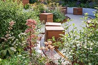 Vue à travers l'espace public, avec des sièges de cube en bois mobiles sur un rail. The Crest Nicholson Livewell Garden, Exposition florale de Hampton Court, 2019.