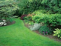 Vue sur pelouse avec parterres de fleurs avec géranium, Hosta et Stachys plantés sous les arbres et arbustes