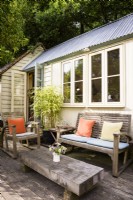 Studio de jardin d'architecte avec coin salon extérieur encadré d'un bambou cultivé en pot dans un jardin de cottage en juin.