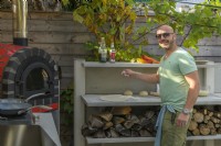 Homme faisant des pizzas dans une cuisine extérieure avec four à pizza rouge et rangement en bois intégré