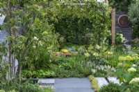 Un endroit pour se retrouver. Hampton Court Flower Festival 2021. Une cour urbaine est plantée dans des tons reposants de vert et de blanc, avec une hauteur ajoutée par une pergola drapée de jasmin étoilé.