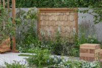 Le Jardin de la Communication. Un refuge tranquille avec des plantations de bois et un écran mural en châtaignier bordé de Delphinium 'Guardian White'.