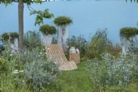 Jardin de la solitude. Une chaise longue est installée au milieu d'une plantation informelle de houx marins, de chardons, d'achillées et de scabieuses. De hautes jardinières en cascade avec des coussins laineux de Muehlenbeckia.