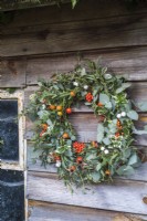 Couronne de Noël accrochée à un hangar avec un thème orange et gris, a des baies oranges et des églantiers, des symphorines blanches et un feuillage gris d'eucalyptus