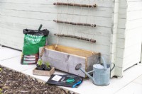 Compost, doublure, arrosoir, ciseaux, étiquettes de plantes, semis, graines disposées à côté de l'auge