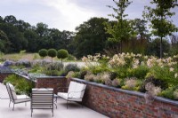 Terrasse contemporaine encadrée d'un parterre planté d'Allium cristophii et d'Hemerocallis 'Catherine Woodbury' en juillet.