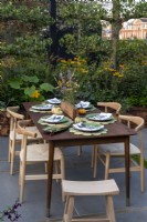 Le Parsely Box Garden est conçu pour les réceptions en plein air. La table sur la terrasse entourée d'arbres fruitiers en espalier, Malus 'Evereste' et Prunus lusitanica qui sont sous-plantés d'herbes, de courgettes et de Rudbeckia fulgida Goldsturm.
