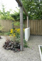 Clôture en bois. Jardin mitoyen avec petit muret blanc et pergola en bois. Surface de gravier. Rudbeckia et Heuchera dans le parterre de fleurs.