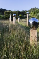 Avenue en prairie de globes en acier inoxydable montés sur des piliers en bois avec un environnement reflété dans les globes. Juillet, été.