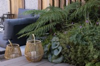 terrasse en bois avec bougeoirs décoratifs en canne. Parterre de fleurs comprend Brunnera 'Jack Frost' et fougère, Polystichum polyblepharum