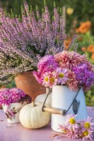 Chrysanthèmes roses et pêche affichés dans un pot en émail sur une table avec des citrouilles blanches, Erica en pot et tasse de thé