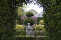 Une statue de chérubin en pierre sculptée baroque entourée d'une haie taillée et d'une topiaire d'if dans le jardin de sculptures à Thenford Gardens and Arboretum, Thenford, Banbury, Oxfordshire, UK